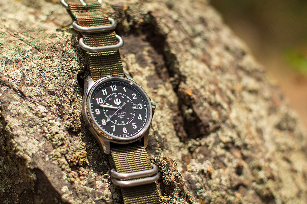 A green zulu strap with an Automatic Field Watch is draped over a textured rock.