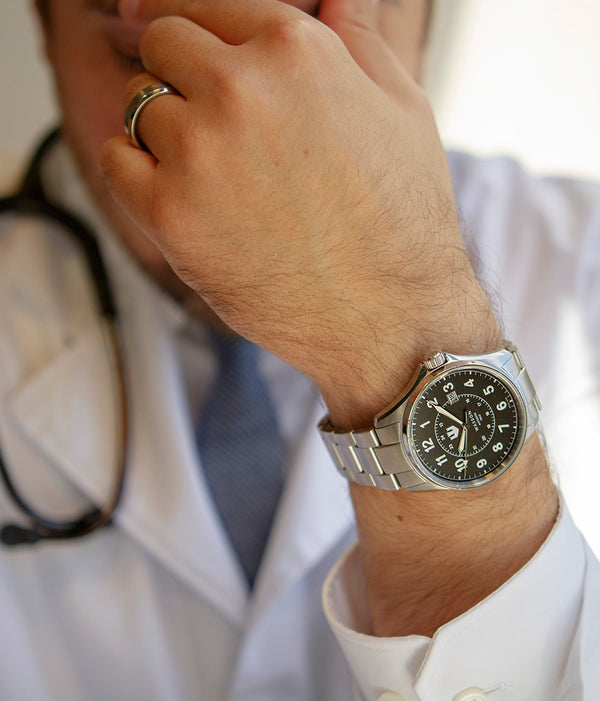 A closeup of a doctor resting his head in his hand while wearing a Swiss-made, stainless steal Wasson Automatic Field Watch. 