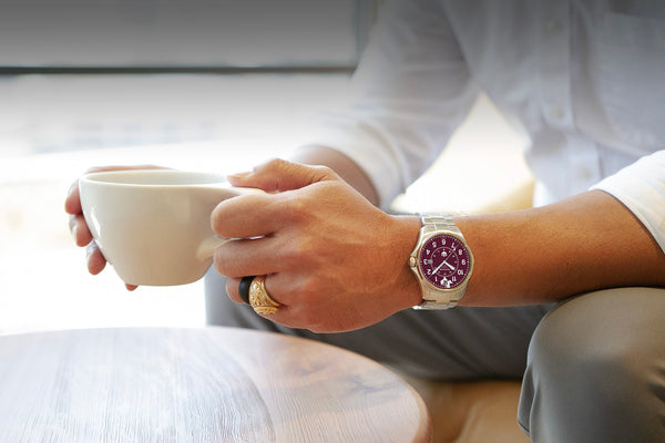 Special edition maroon dial Wasson Automatic Field Watch shown on the wrist of a businessman wearing a Texas A&M ring and holding a cup of coffee. 