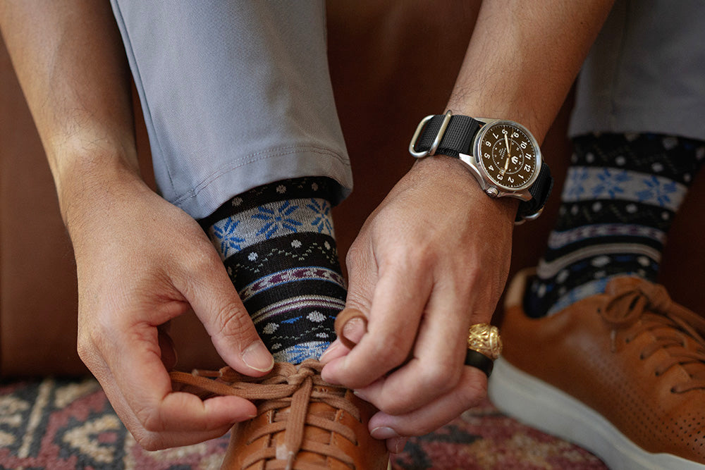 Closeup of a man tying his shoe. He is wearing a Wasson Automatic Field Watch with a black nato strap on his wrist.