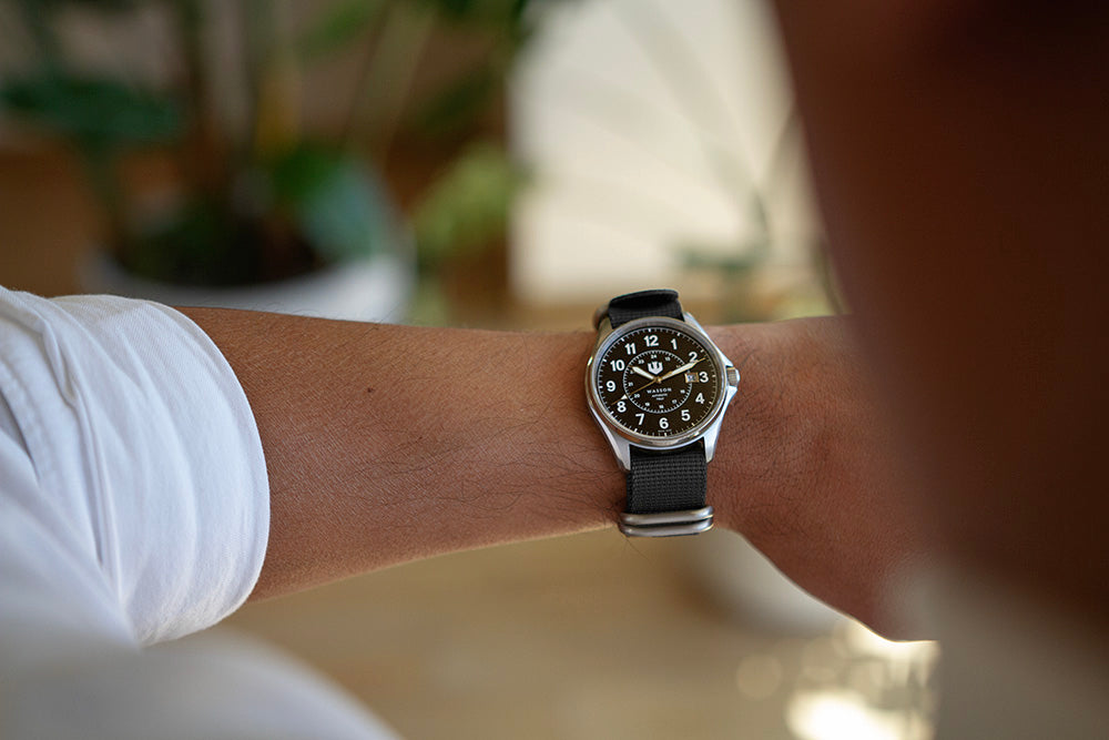 Over the shoulder shot of a man checking his watch for the time. He is wearing a Wasson Watch with black zulu strap.