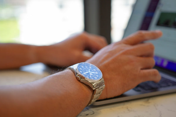 Closeup of a man's hands on the keyboard of a laptop. He is wearing a stainless steel, Swiss-made automatic field watch on his right wrist.