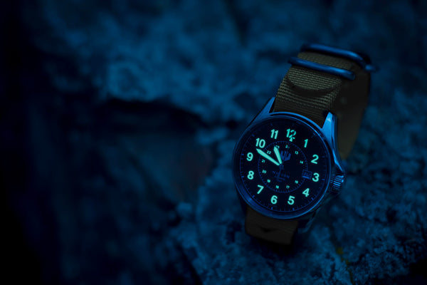 A night shot of a Swiss made Automatic Field Watch sitting on a rock. The numbers and hands are glowing.