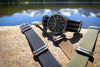 A Wasson Watch sits atop a rock with a lake in the background. There are three zulu straps laying on the rock around it.