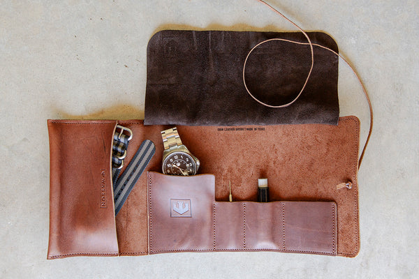 A brown leather tool roll is laid open. It shows four pockets of various sizes. In one pocket is the watch, another pocket houses the extra nylon strap, a link removal tool is in a different pocket, and the spring bar removal tool is in a fourth pocket.