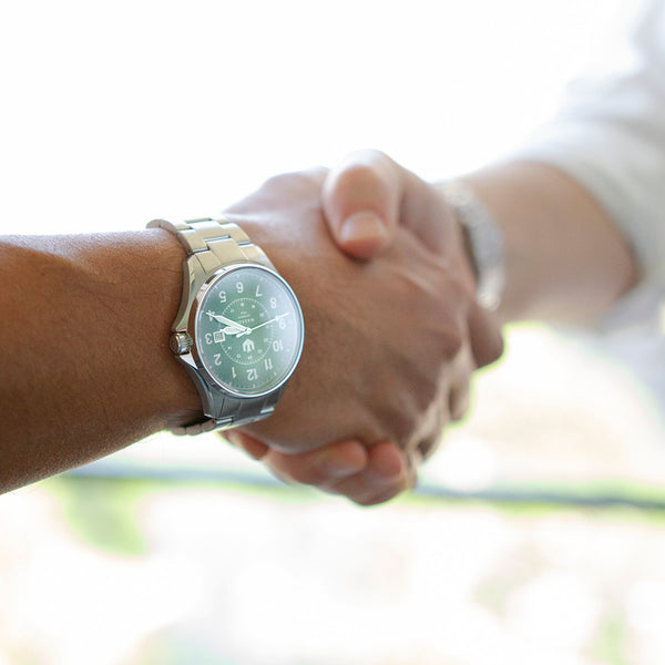 A closeup of two men shaking hands, and one of them wears a stainless steel, Swiss-made watch.