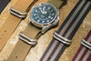 A maroon and gray zulu strap is shown in the corner of the image. There are three other zulu straps in the photo with a Wasson Watch on a green strap.