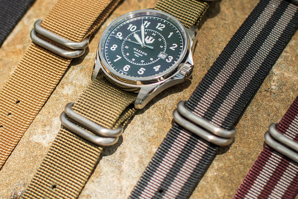 A maroon and gray zulu strap is shown in the corner of the image. There are three other zulu straps in the photo with a Wasson Watch on a green strap.