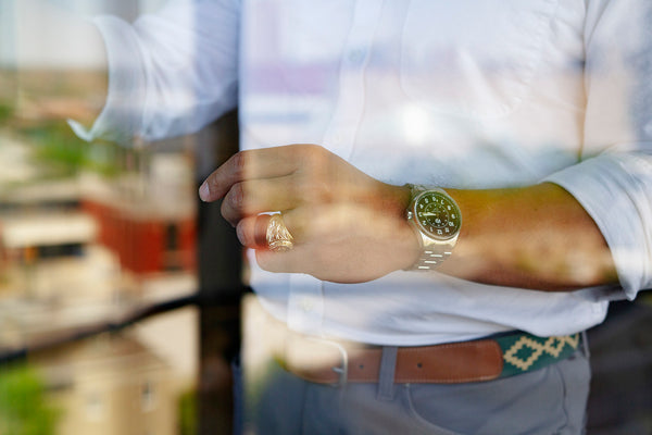 An abstract, closeup image of a man's torso shot through a pain of glass. The man wears a white button-down shirt with his left arm raised slightly. He wears a stainless steel automatic watch, and you can see the reflection of a city scape in the glass.