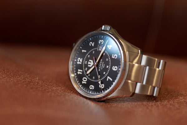 Closeup of a Swiss-made, stainless steel automatic watch laying on its side on a tan leather surface.